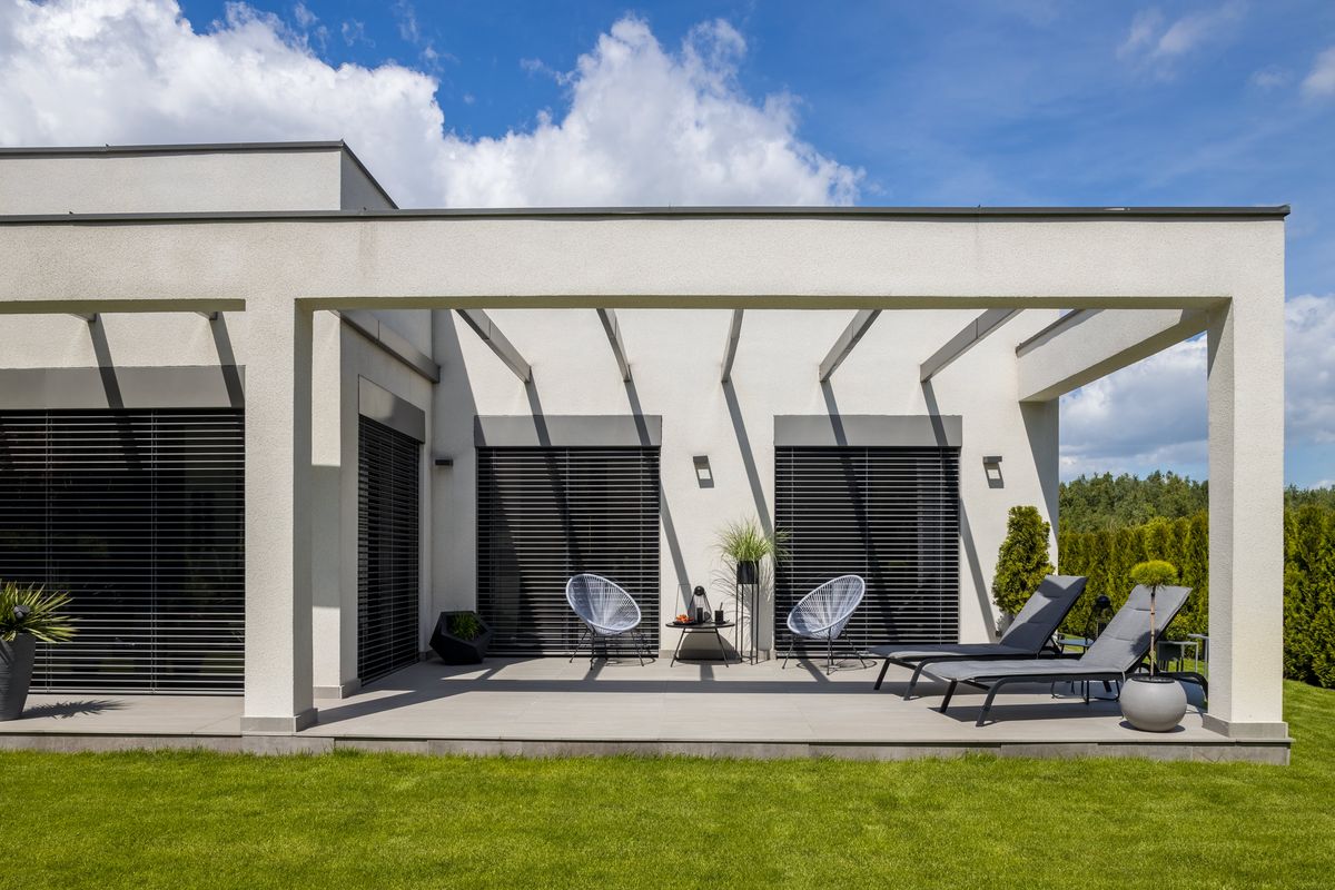 Vivienda unifamiliar blanca con pérgola sobre el porche y jardín de césped