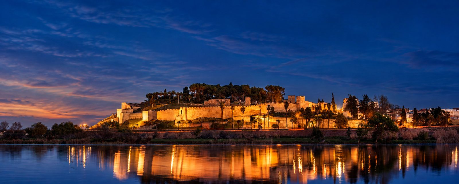 Alcazaba de Badajoz iluminada al anochecer y reflejada en el río Guadiana
